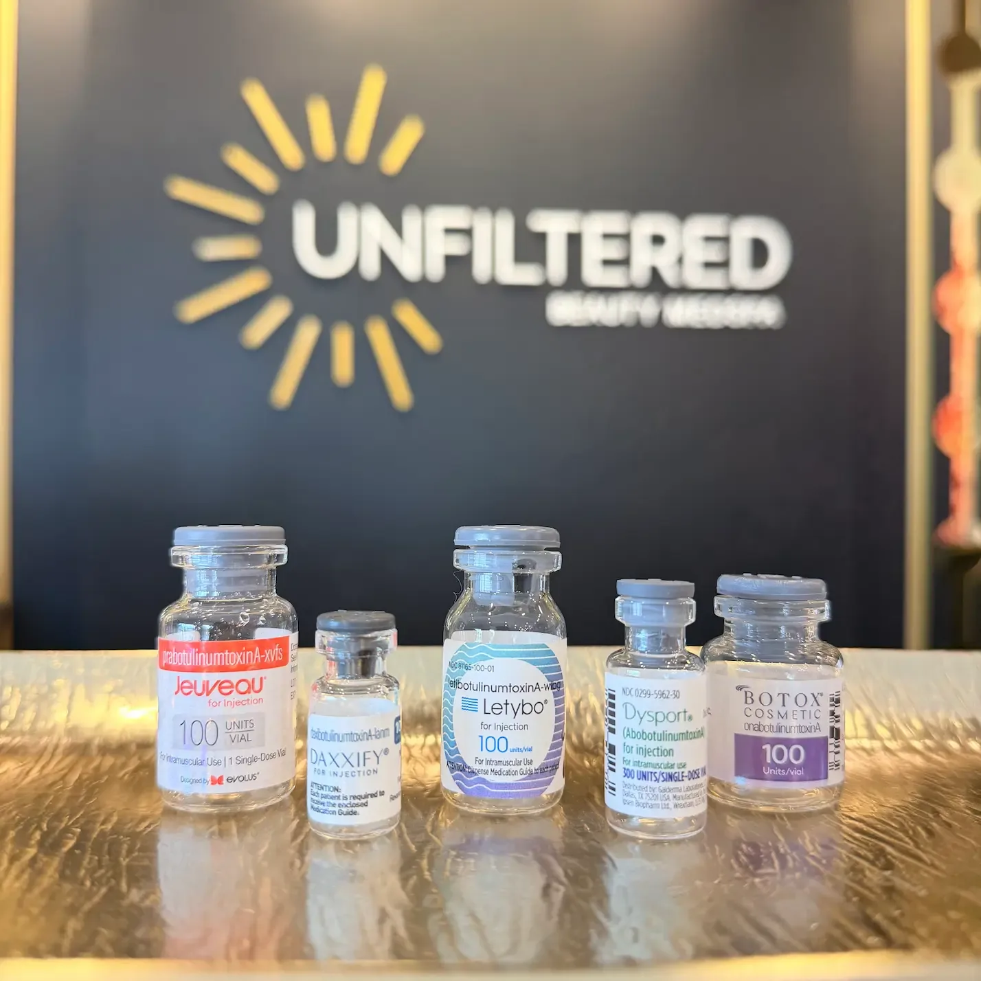 Neurotoxin vials — Botox, Dysport and Letybo — lined up under the studio's logo wall